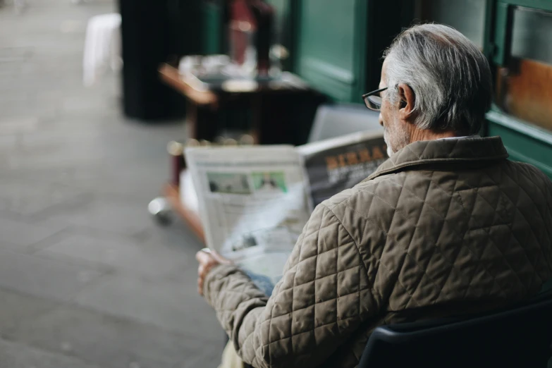 a man sitting on a bench reading a newspaper, a photo, pexels contest winner, private press, dark grey haired man, profile image, wearing reading glasses, covered in