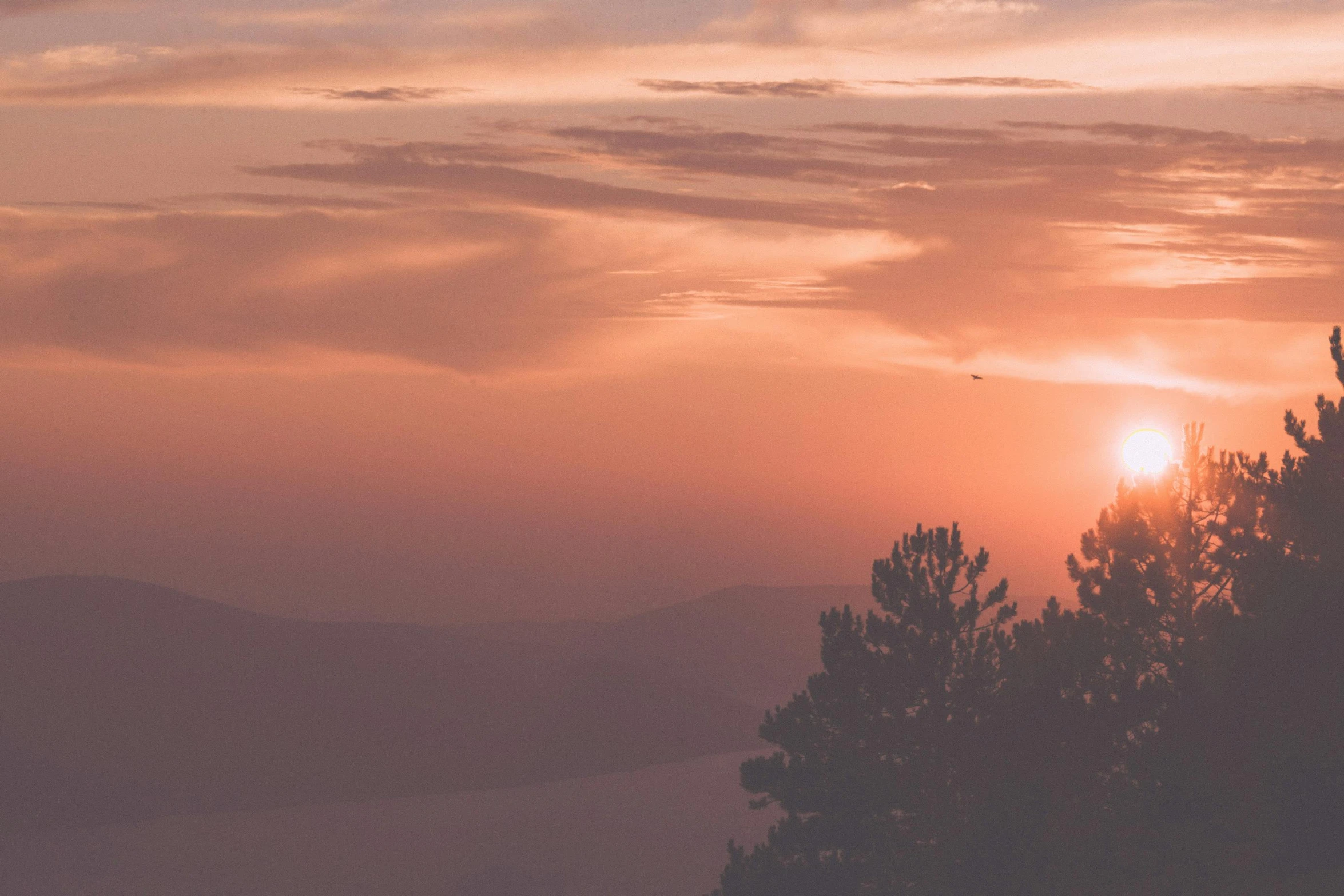 a plane flying over the top of a mountain at sunset, pexels contest winner, romanticism, in a sunset haze, big bear lake california, overlooking a valley with trees, pink sun