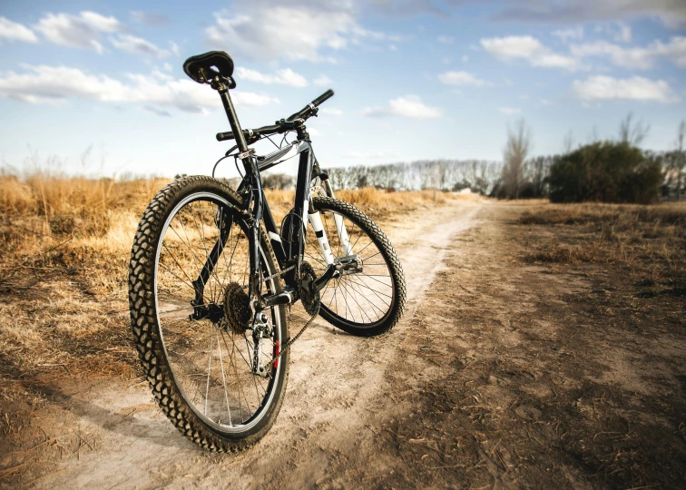 a bicycle parked on the side of a dirt road, riding a bike