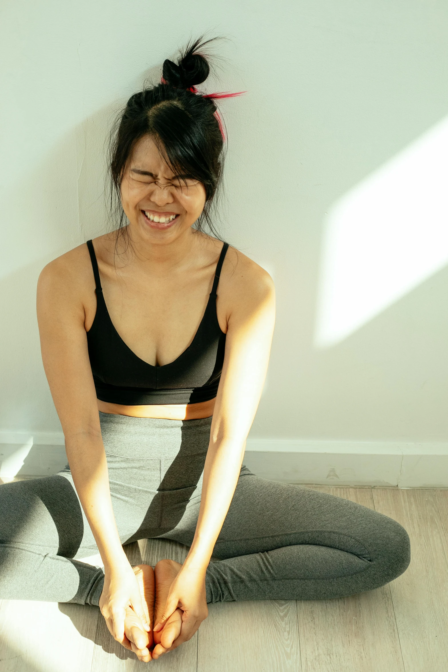 a woman sitting on the floor with her legs crossed, inspired by helen huang, head bent back in laughter, dim dingy gym, profile image, wearing a low cut tanktop