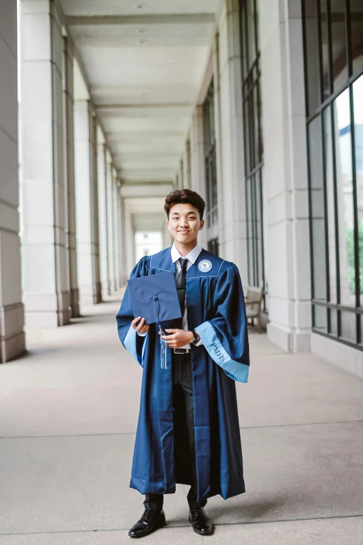 a man in a graduation gown posing for a picture, a portrait, by Robbie Trevino, unsplash, costume with blue accents, lulu chen, full length photo, very handsome