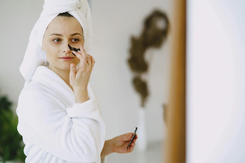 a woman standing in front of a mirror with a towel on her head, trending on pexels, complimentary eyeliner, manuka, wearing robe, thumbnail