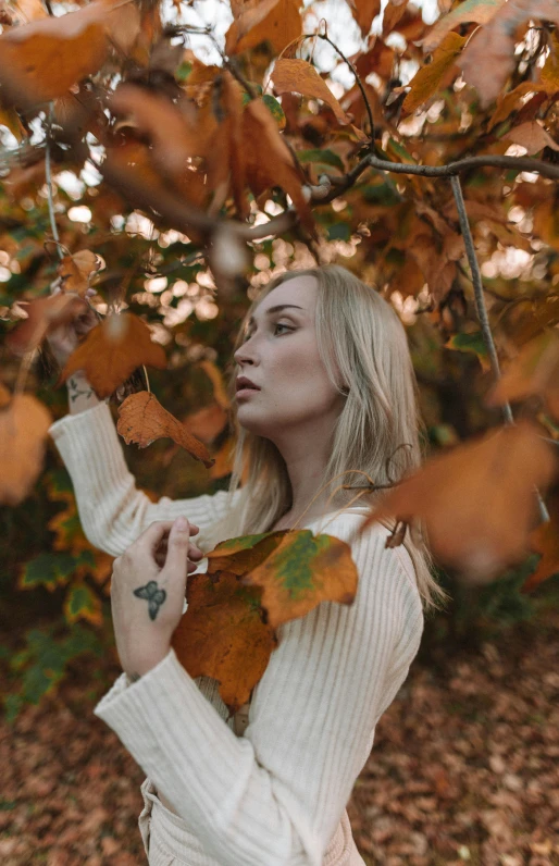 a woman standing in front of a tree with leaves, trending on pexels, aestheticism, blonde swedish woman, various posed, made of leaves, color footage