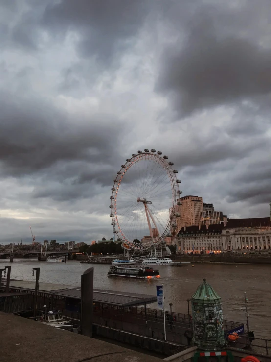 a large ferris wheel sitting on the side of a river, ominous clouds, 80s london city, ☁🌪🌙👩🏾, 2022 photograph