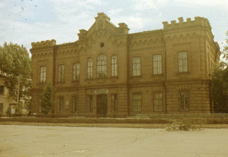 a large brick building sitting on the side of a road, a colorized photo, inspired by György Rózsahegyi, private academy entrance, brown, preserved historical, opalescent palace