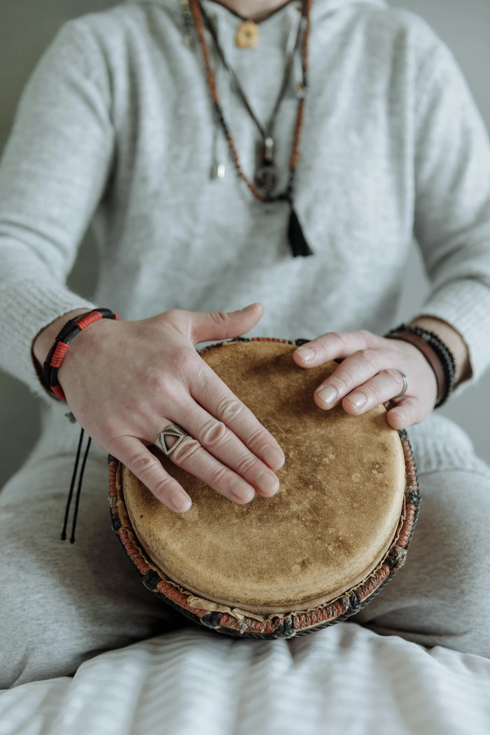 a man sitting on top of a bed holding a drum, by Nina Hamnett, trending on pexels, hurufiyya, photo of a hand jewellery model, dance meditation, sitting with wrists together, winter