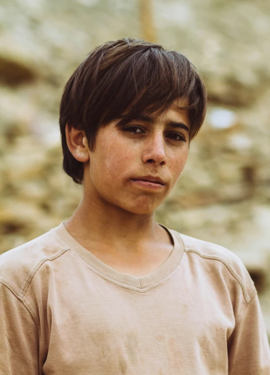 a young boy standing in front of a stone wall, dirty olive skin, awardwinning movie still, 14 yo berber boy, caramel. rugged