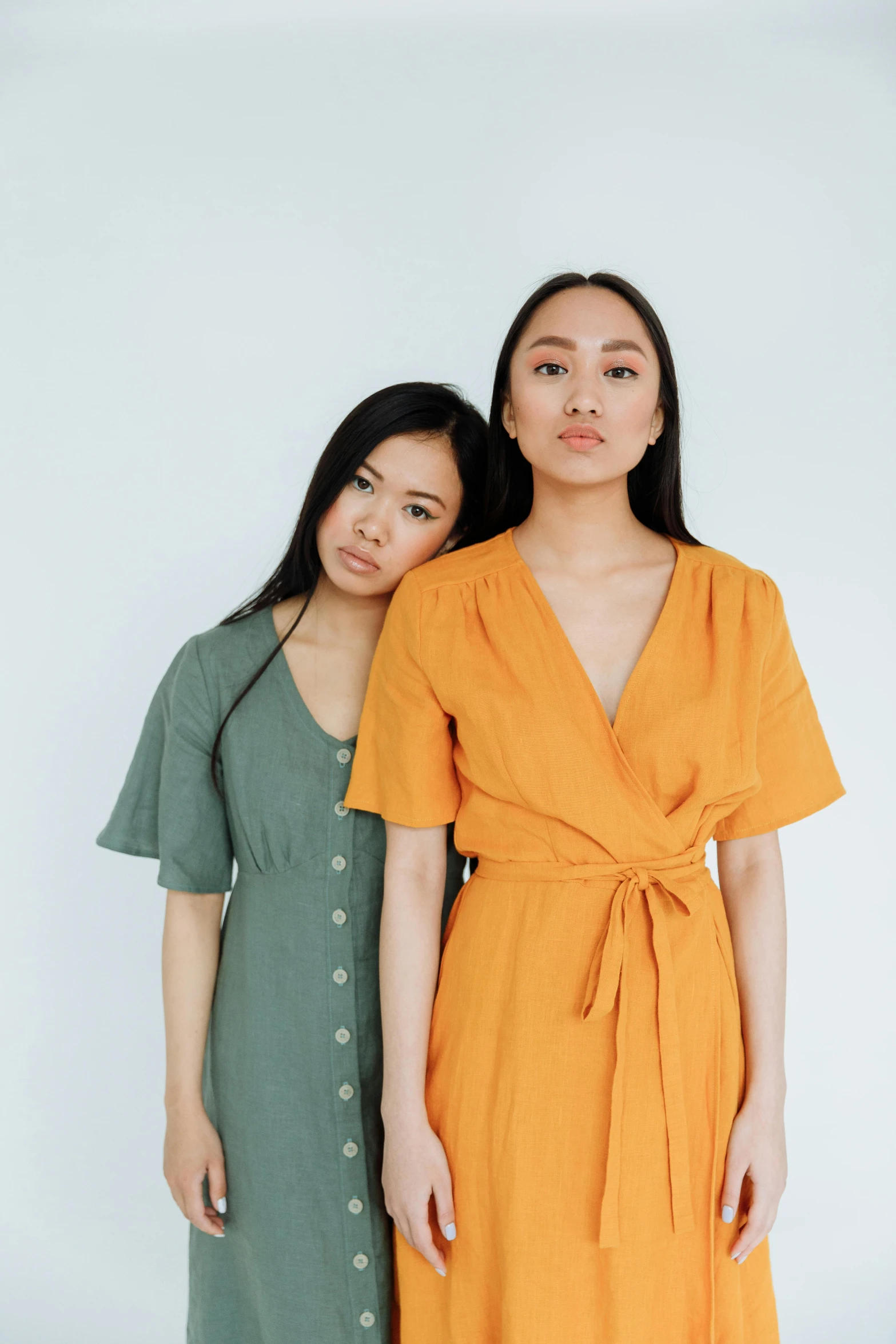 two women standing next to each other in dresses, inspired by Wang Duo, unsplash, plain background, green and yellow, asian woman, orange jumpsuit