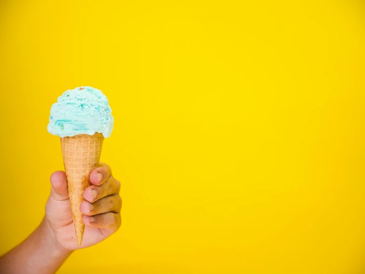 a hand holding an ice cream cone against a yellow background, by Dan Content, trending on unsplash, blue and cyan scheme, background image, blue wall, 🐿🍸🍋