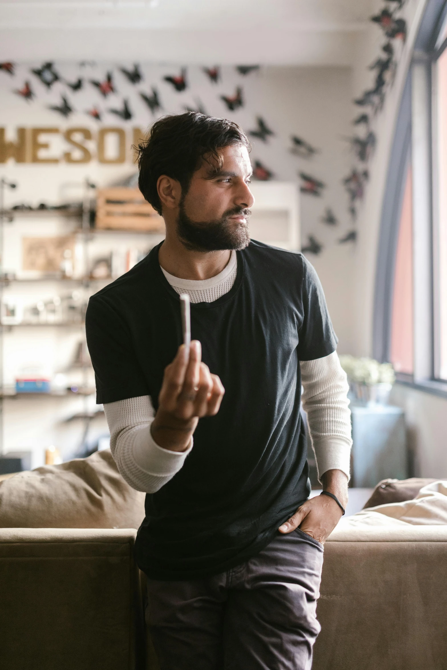 a man standing in a living room next to a couch, holding a small vape, 9 9 designs, wearing adidas clothing, alessio albi