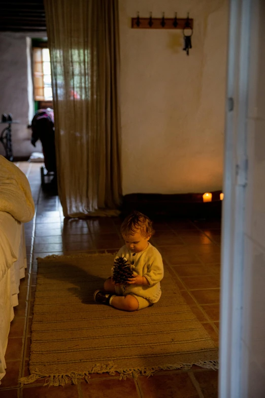 a small child sitting on a rug in a room, by Elsa Bleda, process art, cozy candlelight, slate, ocher, spa