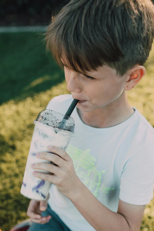 a young boy sitting in the grass drinking a drink, an album cover, pexels, drink milkshakes together, closeup - view, made of drink, filled with bioluminescence