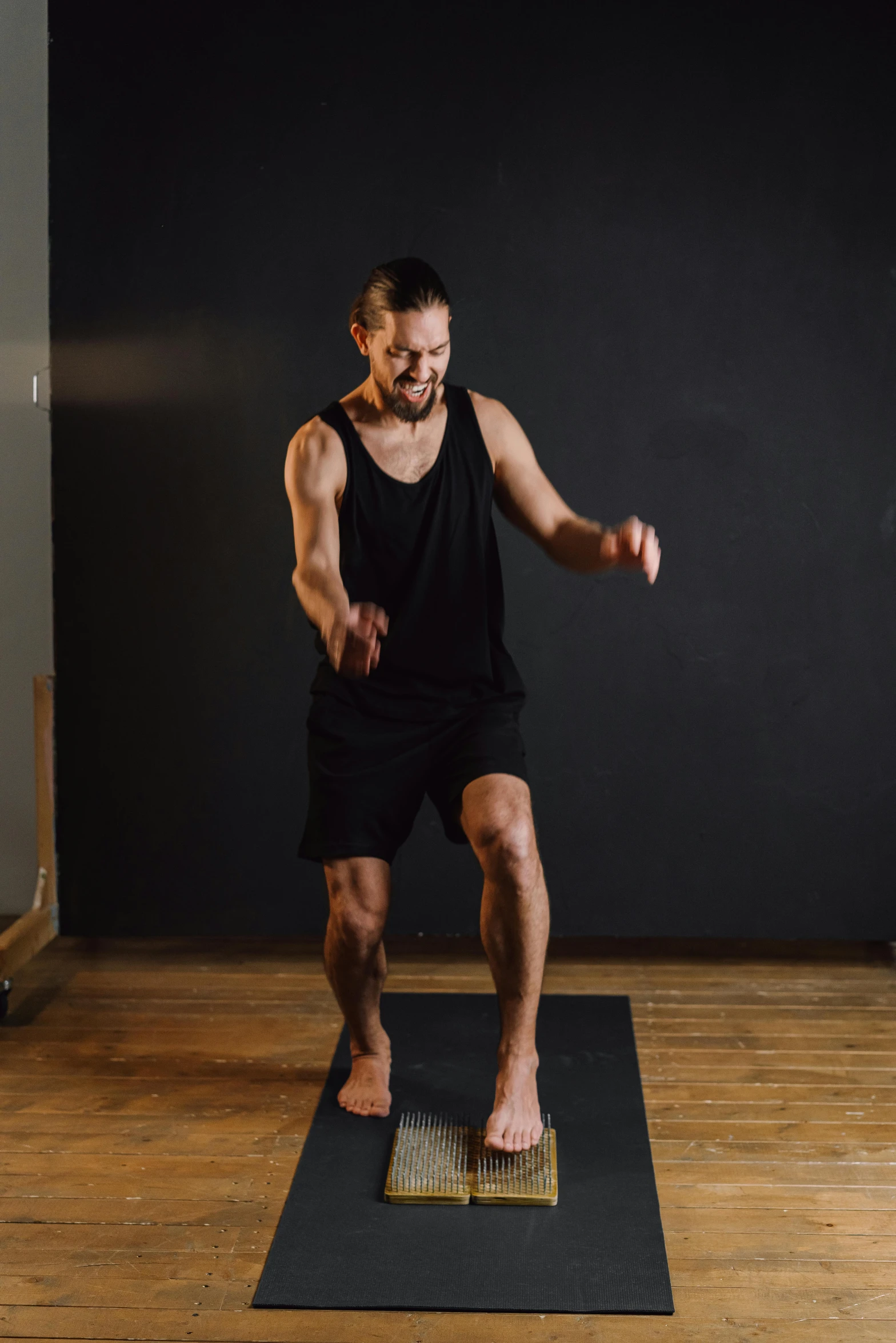 a man in a black tank top standing on a yoga mat, figuration libre, stomping, dan ouellette, shows a leg, ouchh and and innate studio