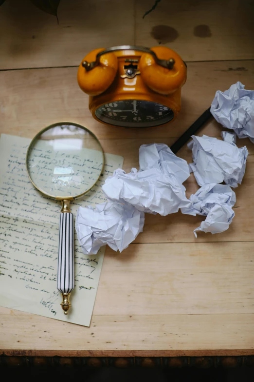 a wooden table topped with a pile of paper and a magnifying glass, wrinkly, writing a letter, circular, prop