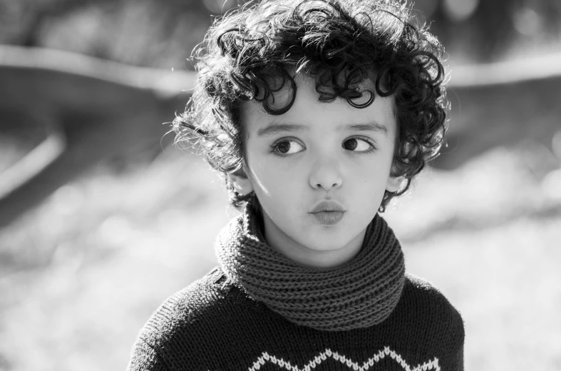 a black and white photo of a young boy, by irakli nadar, pexels, black curly hair, black wool sweater, cute pout, photo realistic”