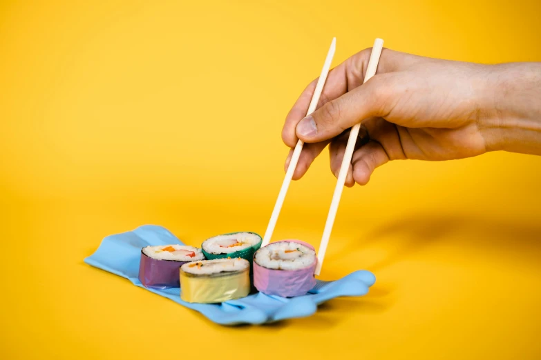 a person holding chopsticks over a plate of sushi, by Julia Pishtar, plasticien, yellow and purple color scheme, blue, cardboard, stockphoto