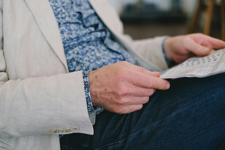 a close up of a person reading a newspaper, by Carey Morris, unsplash, dressed in 1970s menswear, sitting with wrists together, middle aged man, wearing a cardigan