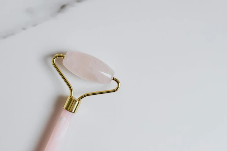 a rose quartz roller on a marble surface, trending on pexels, long thick shiny gold beak, white background, spoon placed, old skin