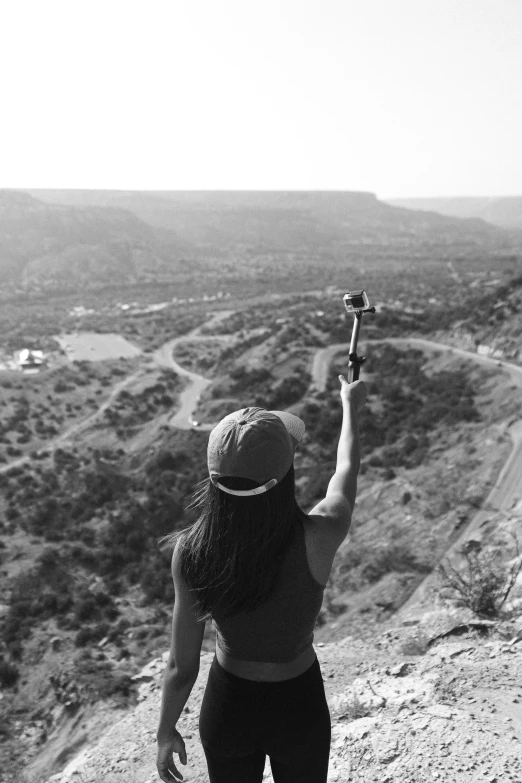 a black and white photo of a woman holding a skateboard, a black and white photo, by Altichiero, top of a canyon, selfie!!!!!, crane shot, ox