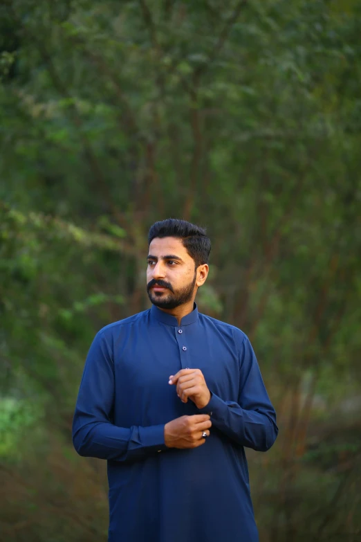 a man standing in front of a forest, an album cover, by Riza Abbasi, pexels contest winner, hurufiyya, he wears a blue shirt, wearing a kurta, profile image, programming