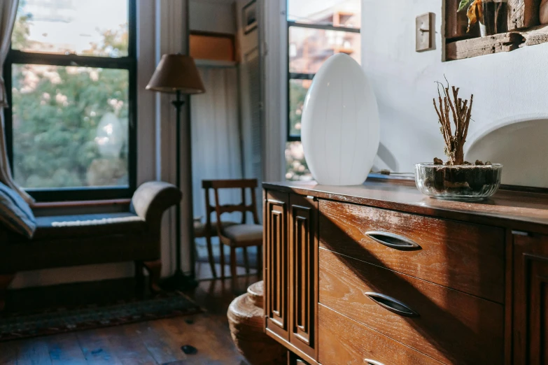 a wooden dresser sitting in a living room next to a window, inspired by Constantin Hansen, trending on unsplash, arts and crafts movement, magnificent oval face, rundown new york apartment, samsung smartthings, white ceramic shapes