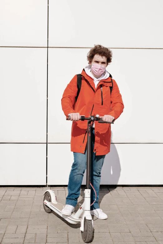 a boy in an orange jacket riding a scooter, trending on pexels, happening, wearing facemask, standing, college, non-binary