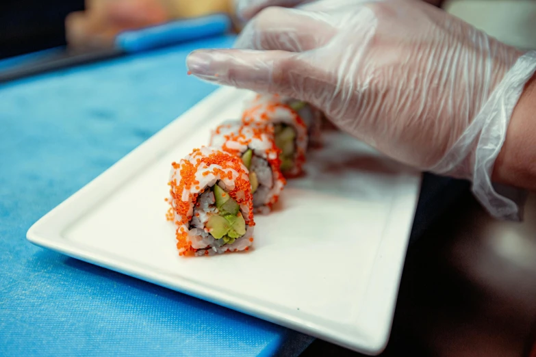 a white plate topped with sushi on top of a blue table, hand on table, profile image