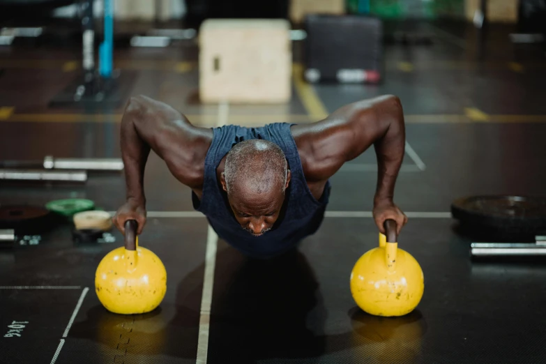 a man doing a push up with two yellow kettlebells, by Lee Loughridge, pexels contest winner, man is with black skin, spherical body, aged 4 0, thumbnail