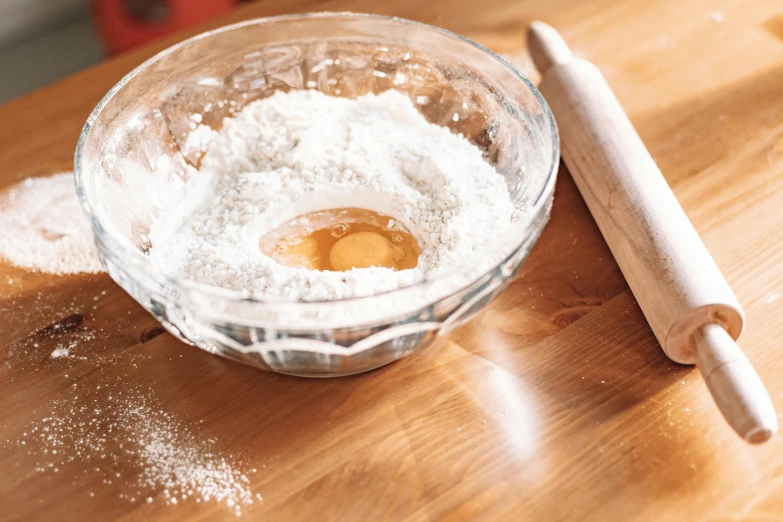 a wooden table topped with a bowl of flour and a rolling pin, trending on pexels, glass tableware, thumbnail, spiraling, bottom angle