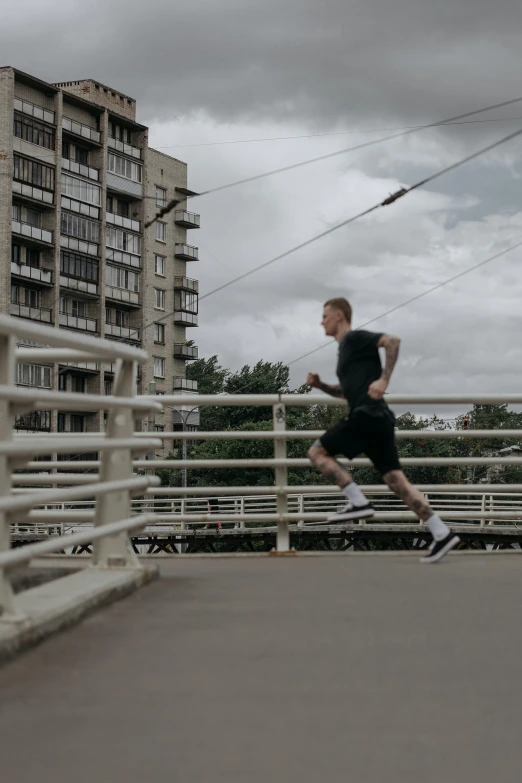 a man running across a bridge on a cloudy day, inspired by Alexander Litovchenko, unsplash, realism, low quality footage, street of moscow, local gym, 8 k film still