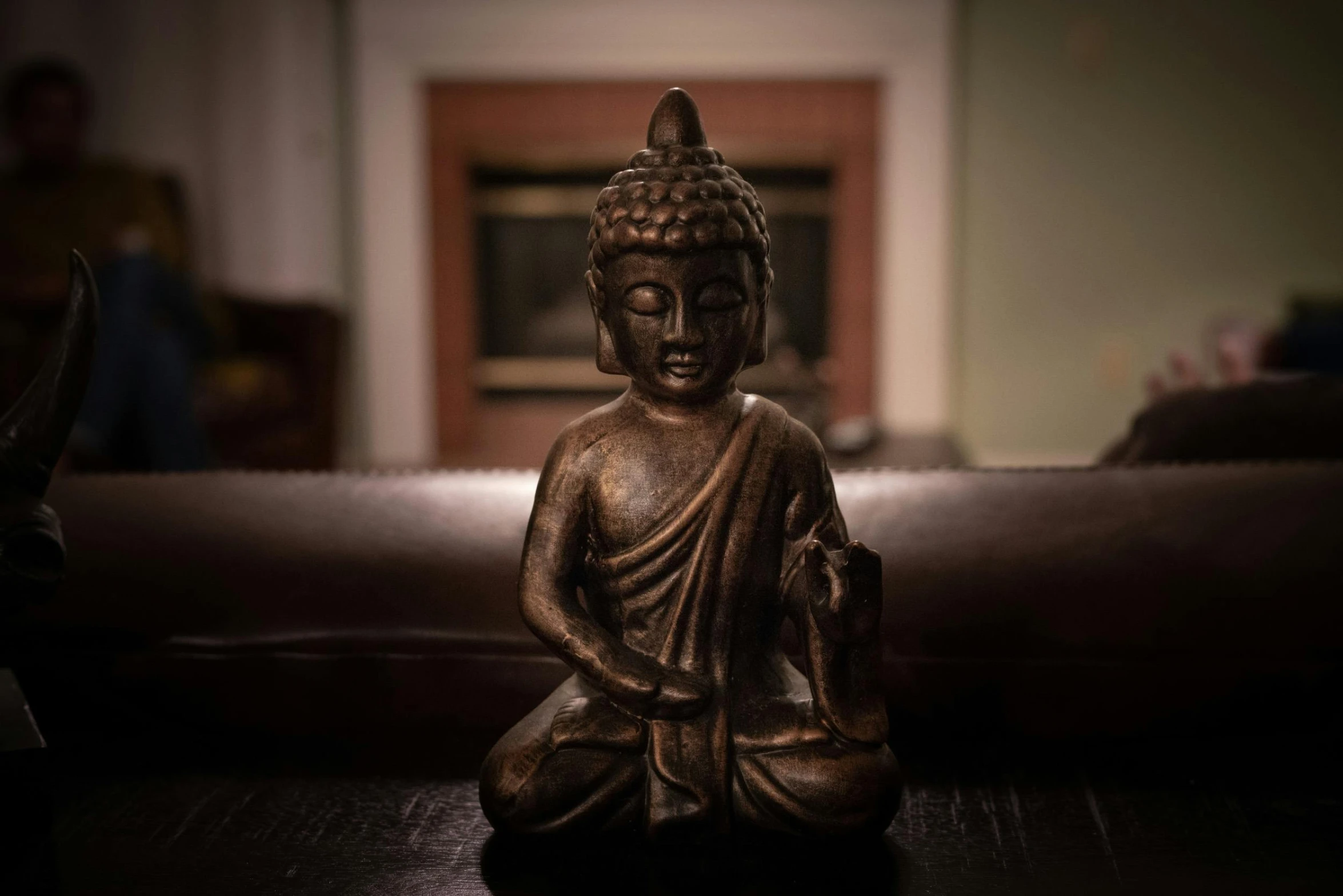 a buddha statue sitting on top of a wooden table, sitting on a couch, shot on sony a 7 iii, brown, eye - level medium - angle shot
