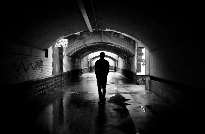 a black and white photo of a person walking through a tunnel, sad men, josh black, dominance, standing alone