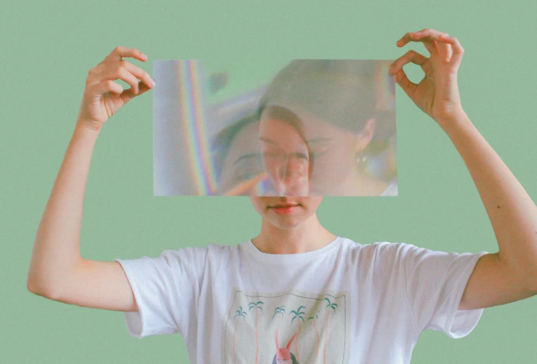 a person holding up a picture in front of their face, inspired by Anna Füssli, pexels contest winner, holography, wearing a t-shirt, muted colors with minimalism, refracted, opaque visor