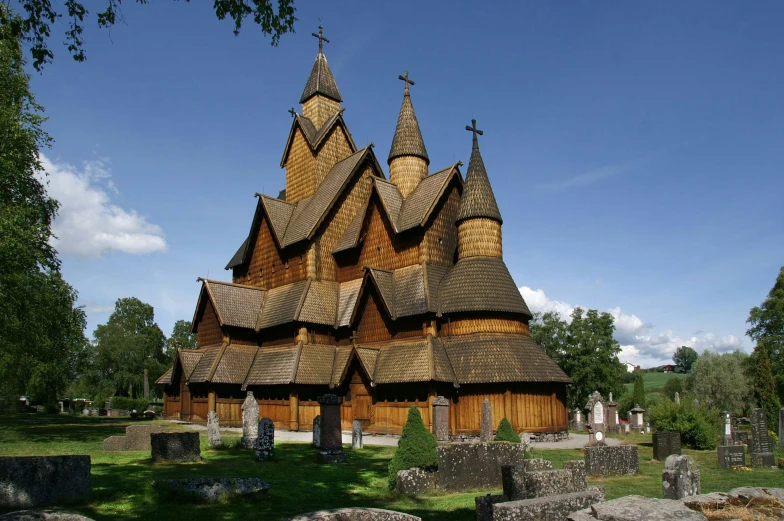a large wooden church sitting on top of a lush green field, inspired by karlkka, romanesque, asymmetrical spires, exterior, well preserved, smoldering