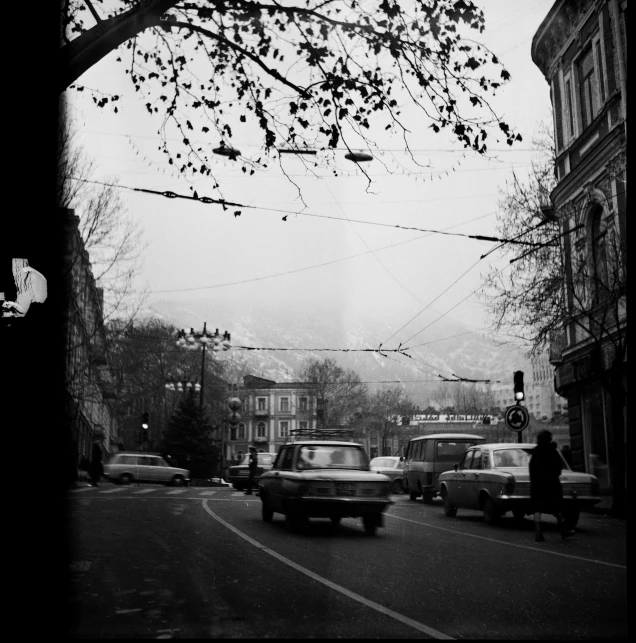 a black and white photo of a city street, by Henryk Rodakowski, mountain, car, portait image, trees in the background