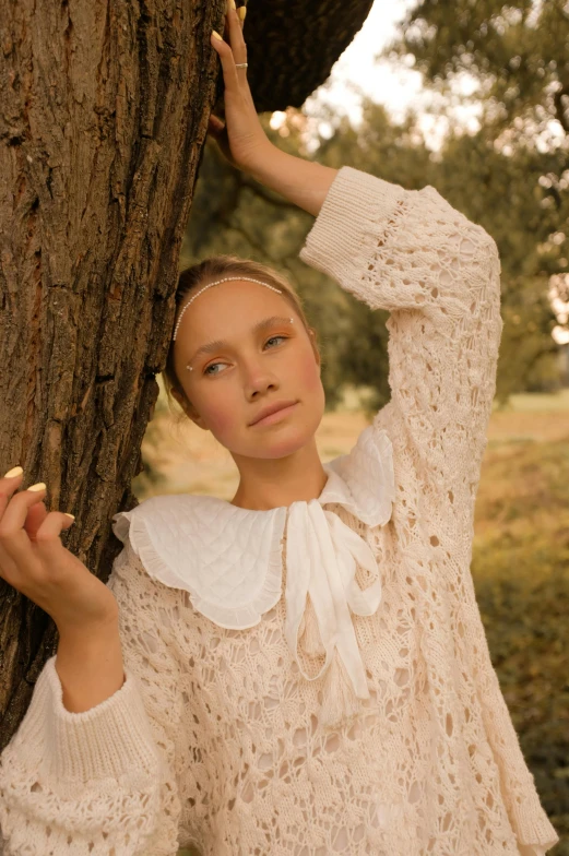 a woman leaning against a tree in a field, inspired by Amalia Lindegren, trending on pexels, renaissance, ivory carved ruff, big collar, white and light-pink outfit, natali portman