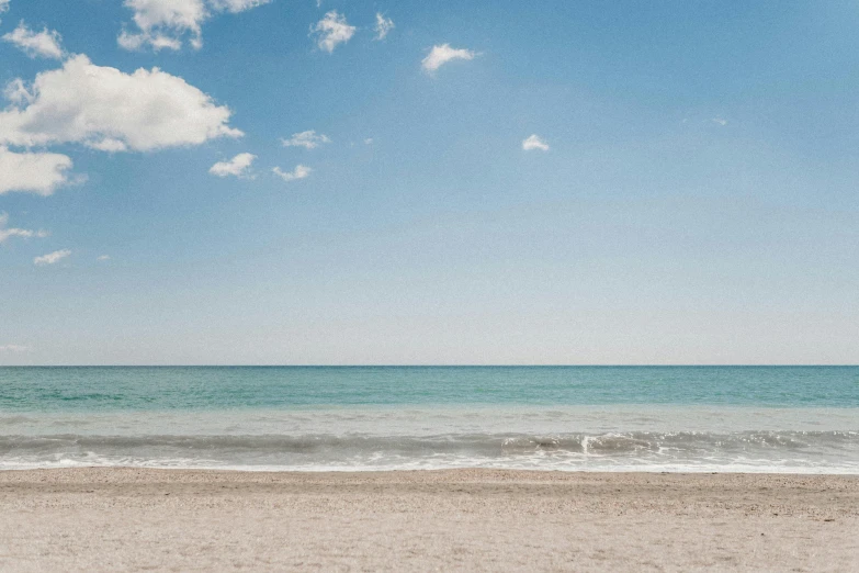 a man standing on top of a sandy beach next to the ocean, unsplash contest winner, minimalism, light blue sky with clouds, apulia, glistening seafoam, a photo of the ocean