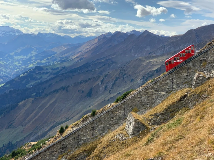 a red train traveling down the side of a mountain, by Werner Andermatt, pexels contest winner, panoramic, fan favorite, epicurious, wheres wally