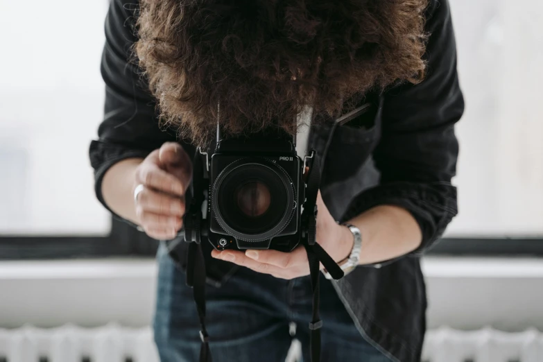 a person taking a picture with a camera, black curly beard, holding it out to the camera, looking down on the camera, over his shoulder