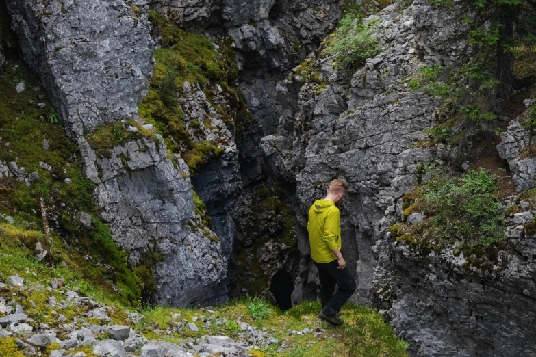 a man in a yellow jacket standing in front of a cave, les nabis, nina tryggvadottir, narrow footpath, in the center of the image, limestone