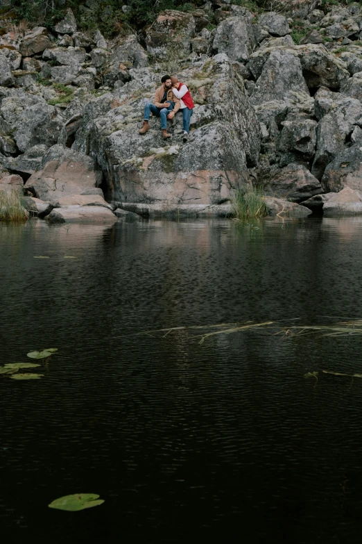 a man and a woman sitting on a rock next to a body of water, by Jaakko Mattila, lava river, minn, teaser, outdoor photo