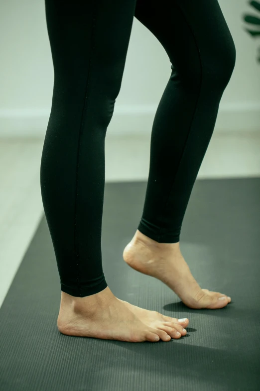 a woman standing on top of a yoga mat, by David Simpson, dribble, jet black leggins, detailed foot shot, looking left, compression