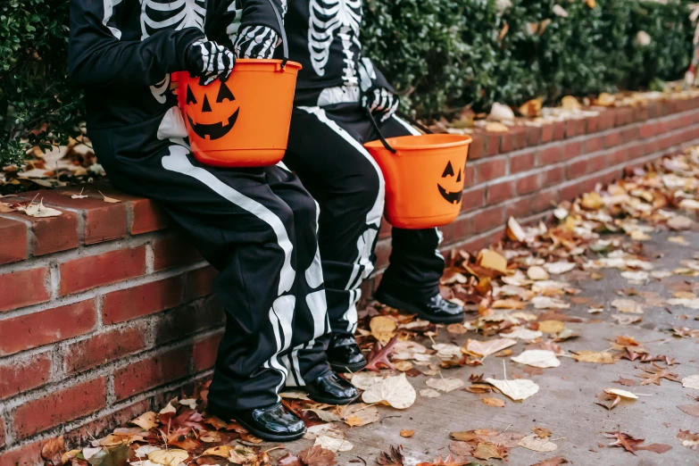 two children in skeleton costumes sitting on a brick wall, by Helen Stevenson, pexels, vanitas, trick or treat, cauldrons, promotional image, leaked image