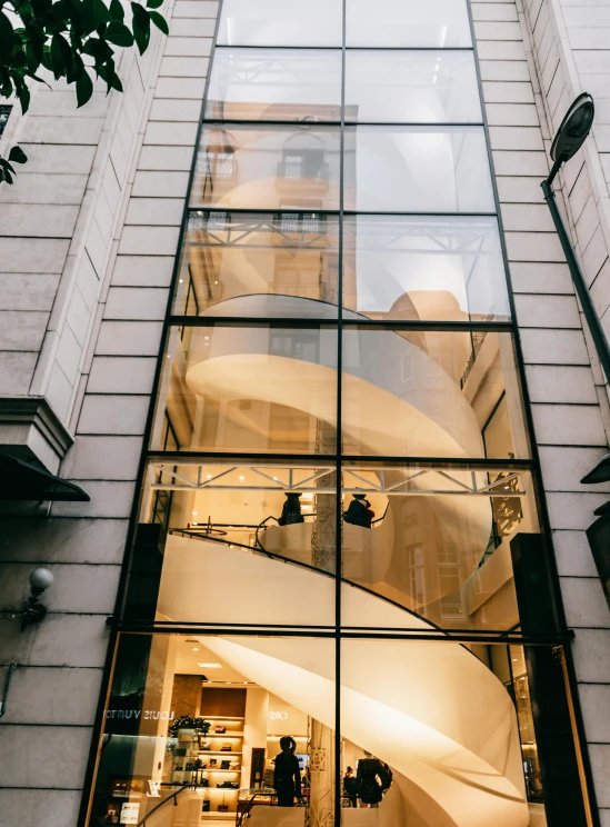 a building with a spiral staircase in front of it, by Nina Hamnett, trending on unsplash, modernism, nesting glass doors, warm lighting inside, taken on iphone 14 pro, in london