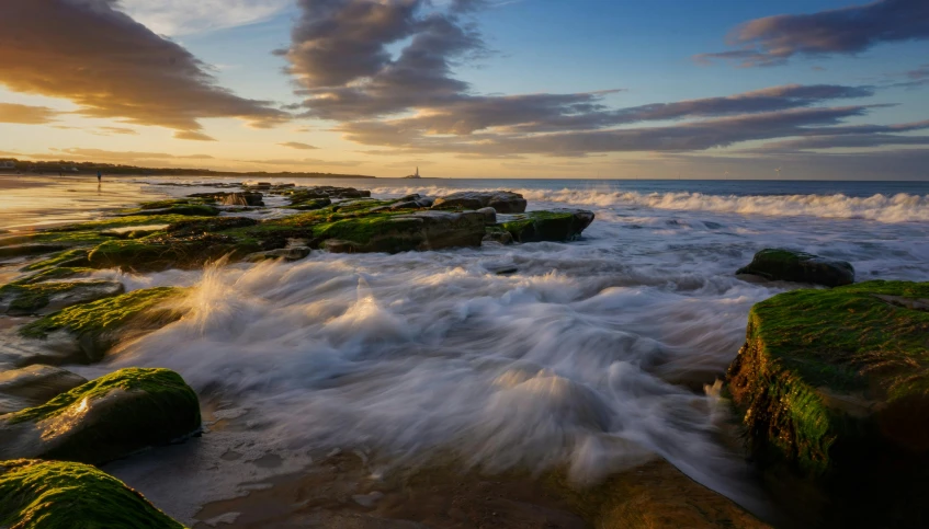 a large body of water sitting on top of a sandy beach, by Robert Sivell, pexels contest winner, waves crashing at rocks, marsden, magic hour photography, rushing water