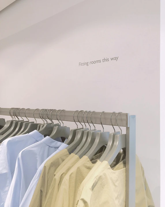 a row of shirts hanging on a rack in a clothing store, an album cover, by Thomas Furlong, postminimalism, white and pale blue, with text, uniform off - white sky, branching hallways