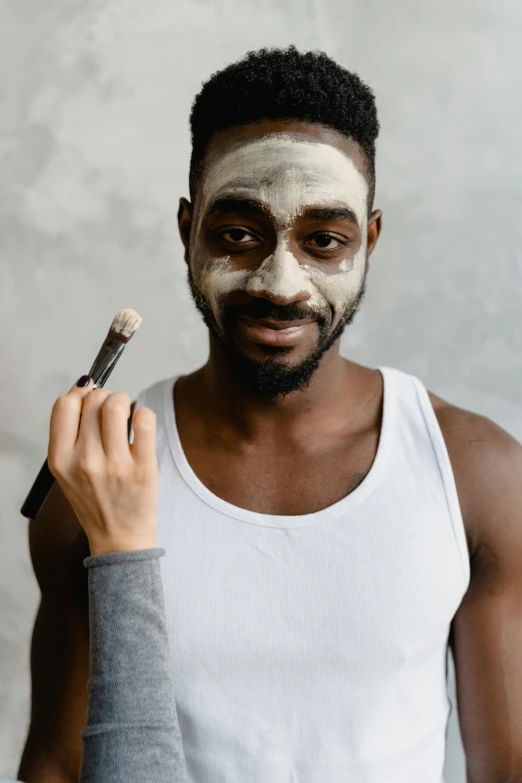 a man is shaving his face with a brush, by Arabella Rankin, trending on pexels, renaissance, yoruba body paint, ski mask, thumbnail, gray anthropomorphic