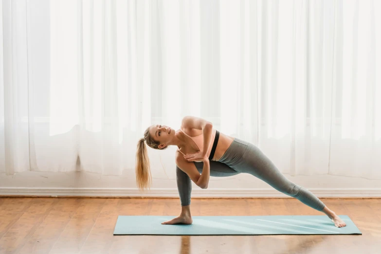 a woman doing a yoga pose on a yoga mat, unsplash, arabesque, background image, leaning against the window, manuka, lizard pose