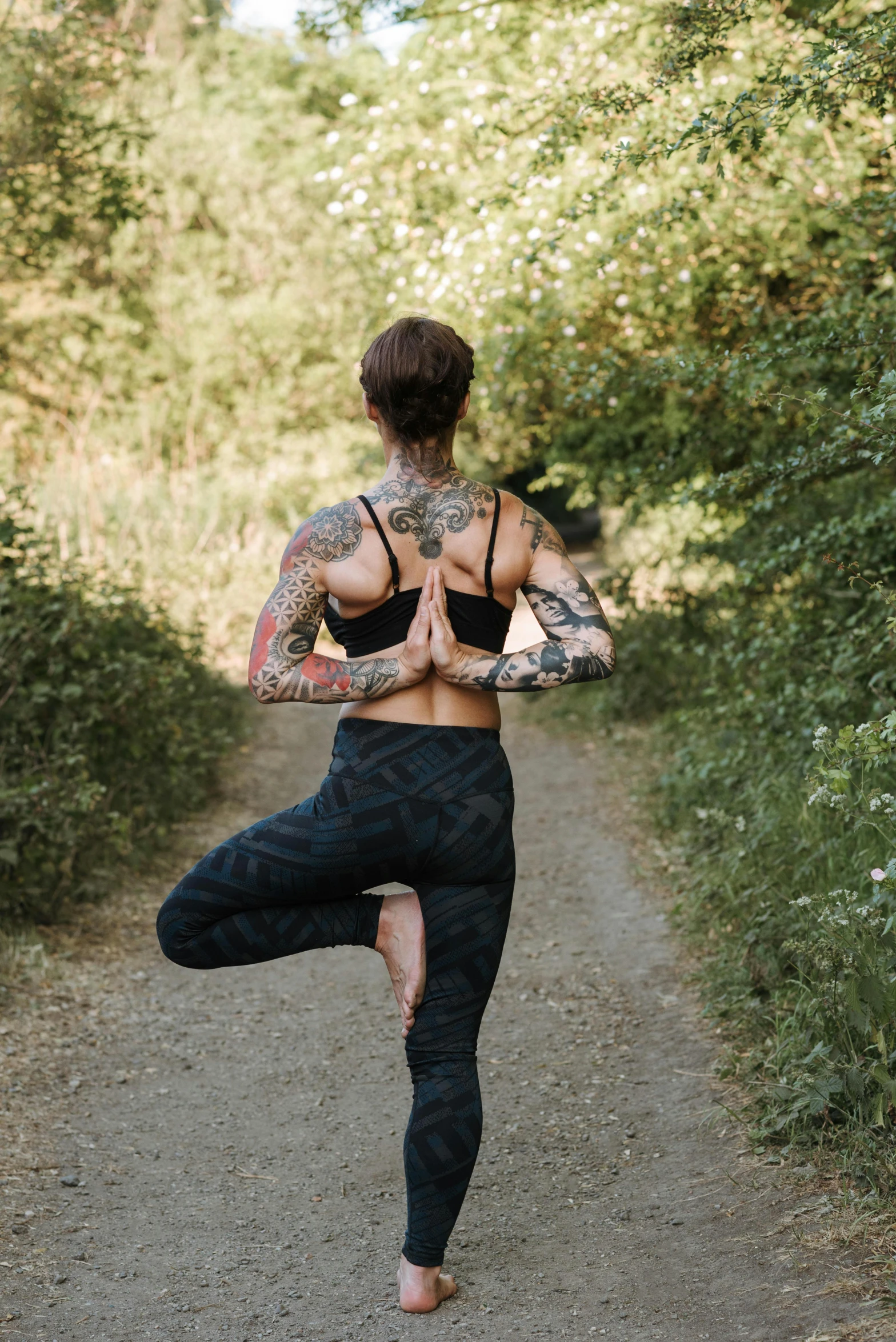 a woman doing yoga on a dirt road, a tattoo, with tattoos, lush surroundings, hero pose, jay bauman