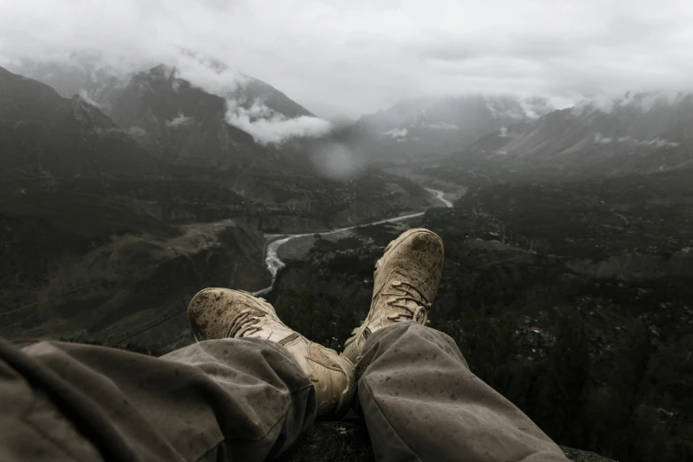 a person sitting on top of a mountain with their feet up, pexels contest winner, wearing military shoes, overcast weather, dying earth, portrait of a rugged ranger